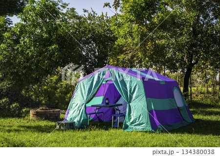 Camping tents at morning, vintage cabin tents, antique oil lamps, retro chairs, and a group of camping tents with outdoor coffee-making facilities on wooden tables in a forest camping area. Camping tents at morning, vintage cabin tents, antique oil lamps, retro chairs, and a group of camping tents with outdoor coffee-making facilities on wooden tables in a forest camping area. 134380038