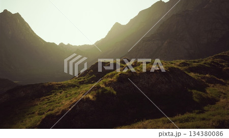 As the sun sets, golden light spills over majestic mountains, illuminating the lush, green terrain of a peaceful valley perfect for nature lovers and adventurers. 134380086