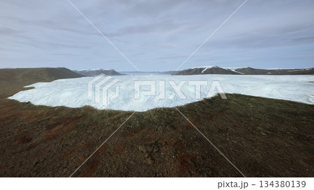 A breathtaking scene shows a vast glacier extending over rocky ground in Iceland. The icy blue surface contrasts beautifully with the earthy tones of the landscape. 134380139