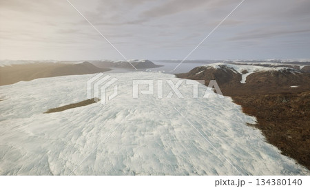 A vast glacier stretches across the landscape under soft morning light. Mountains rise in the distance, creating a stunning backdrop filled with ice and rock formations. 134380140