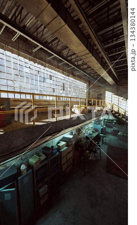 Sunlight illuminates a spacious industrial warehouse filled with equipment and vintage storage. The warm glow creates captivating shadows on the concrete floor, showcasing its history. 134380144