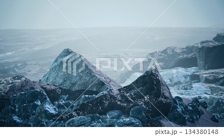 A rugged landscape features sharp, icy rocks amidst a serene, misty atmosphere. Twilight casts a soft glow, revealing shadows and textures on the rocky terrain. A rugged landscape features sharp, icy rocks amidst a serene, misty atmosphere. Twilight casts a soft glow, revealing shadows and textures on the rocky terrain. 134380148