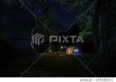Night camping adventure with a cozy tent lit under the starry sky in a summer forest 134380151