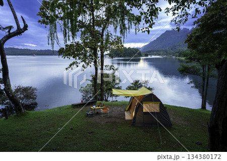 Camping tent on green grass in the morning, antique gas lamps, retro chairs, with outdoor coffee-making facilities on tables in a forest camping area. Camping tent on green grass in the morning, antique gas lamps, retro chairs, with outdoor coffee-making facilities on tables in a forest camping area. 134380172