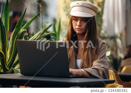 Working with laptop. Beautiful young woman is outdoors of the restaurant by the table Working with laptop. Beautiful young woman is outdoors of the restaurant by the table 134380381