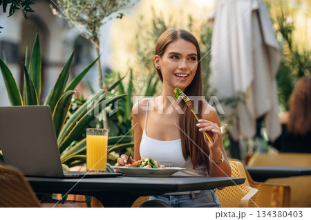 Sitting, eating delicious food. Beautiful young woman is outdoors of the restaurant by the table Sitting, eating delicious food. Beautiful young woman is outdoors of the restaurant by the table 134380403