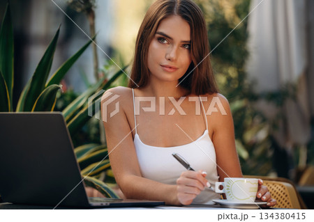 Business deals, with laptop and pen. Beautiful young woman is outdoors of the restaurant by the table 134380415