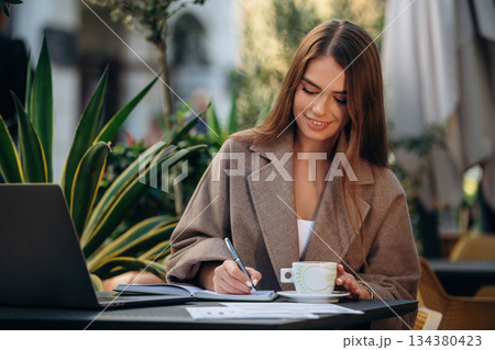 Business deals, with laptop and pen. Beautiful young woman is outdoors of the restaurant by the table 134380423