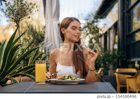 Delicious food. Beautiful young woman is outdoors of the restaurant by the table Delicious food. Beautiful young woman is outdoors of the restaurant by the table 134380498