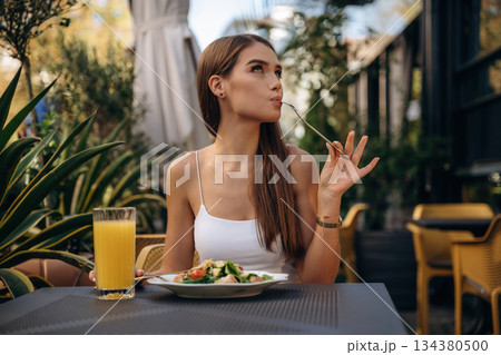 Delicious food. Beautiful young woman is outdoors of the restaurant by the table Delicious food. Beautiful young woman is outdoors of the restaurant by the table 134380500