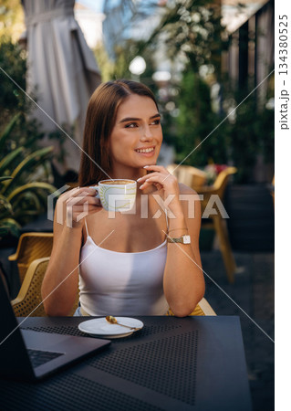 Break time, with coffee. Beautiful young woman is outdoors of the restaurant by the table Break time, with coffee. Beautiful young woman is outdoors of the restaurant by the table 134380525