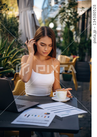 Break time, with coffee. Beautiful young woman is outdoors of the restaurant by the table 134380528