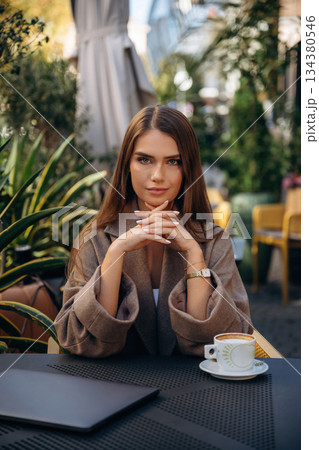 Fresh hot drink in cup. Beautiful young woman is outdoors of the restaurant by the table Fresh hot drink in cup. Beautiful young woman is outdoors of the restaurant by the table 134380546