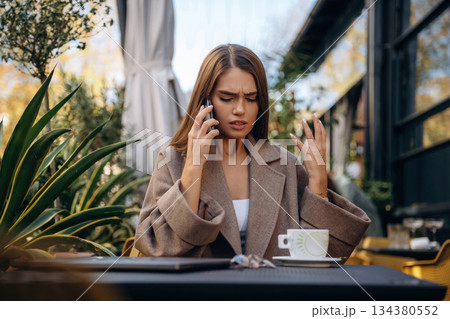 With smartphone. Beautiful young woman is outdoors of the restaurant by the table With smartphone. Beautiful young woman is outdoors of the restaurant by the table 134380552