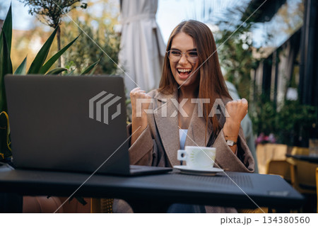 Working with laptop. Beautiful young woman is outdoors of the restaurant by the table Working with laptop. Beautiful young woman is outdoors of the restaurant by the table 134380560