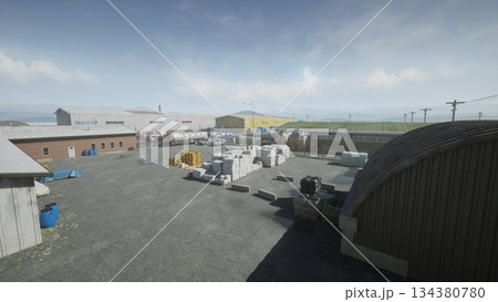 An expansive industrial area features several warehouses filling the landscape, stacked materials, and equipment arranged around a wide gravel lot under a bright, clear sky. 134380780