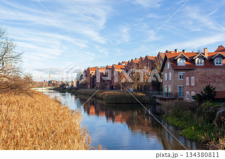 Houses by river with dry grass and clear sky in town during daylight Houses by river with dry grass and clear sky in town during daylight 134380811
