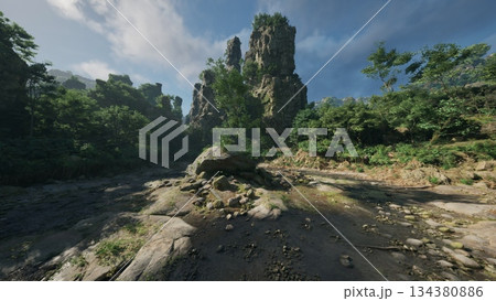 Towering rock formations rise dramatically from a serene riverbank, surrounded by vibrant greenery under a bright blue sky. Peaceful nature invites exploration and reflection. 134380886