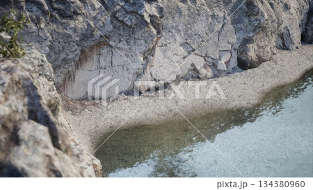 A stunning view showcases a rocky coastline, where clear water meets a pebbled beach. The scene captures the serene beauty of nature during the golden hour of sunset. 134380960