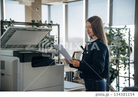 Working with printer. Beautiful woman is in the office 134381154