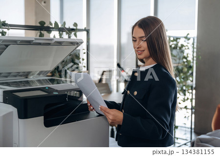 Working with printer. Beautiful woman is in the office 134381155