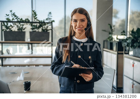 Woman in headphones and with notepad is standing in the office 134381200