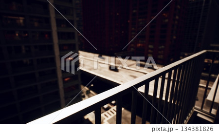 A balcony railing frames a stunning cityscape at night. Bright lights from buildings illuminate the dark sky. The quiet streets below contrast with the vibrant atmosphere above. A balcony railing frames a stunning cityscape at night. Bright lights from buildings illuminate the dark sky. The quiet streets below contrast with the vibrant atmosphere above. 134381826