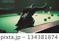 In a dimly lit space, a ram skull with impressive horns rests near a vibrant green pool table. Colorful balls are scattered, creating an intriguing contrast in this atmospheric scene. 134381874