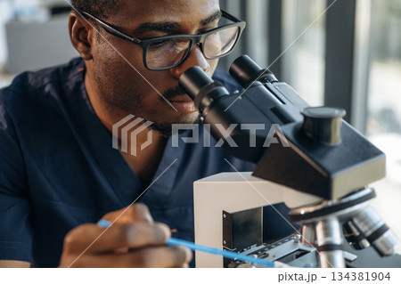 Focused on job. Scientist is working indoors, microscope is on the table Focused on job. Scientist is working indoors, microscope is on the table 134381904