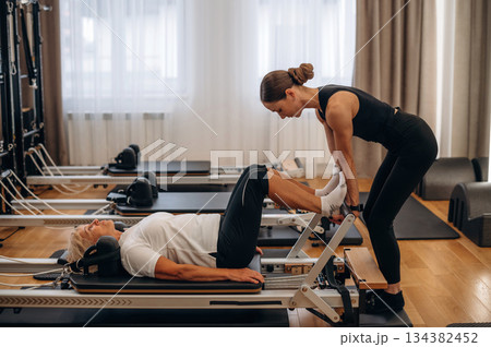 Legs exercise. Female trainer is helping old woman 134382452