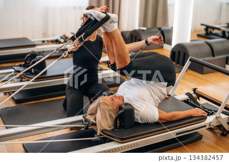 Laying down and doing legs exercise. Female trainer is helping old woman Laying down and doing legs exercise. Female trainer is helping old woman 134382457