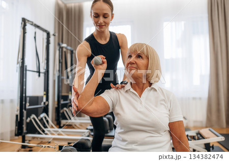 How to lift the dumbbell. Female trainer is helping old woman to exercise How to lift the dumbbell. Female trainer is helping old woman to exercise 134382474