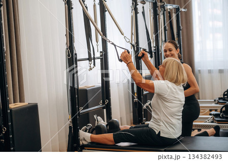 Using training equipment. Female trainer is helping old woman to exercise 134382493