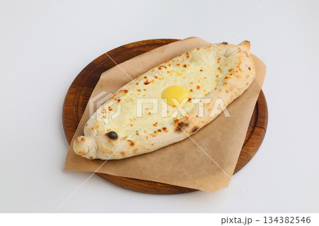 Traditional georgian pastry - adjarian khachapuri with cheese and raw yolk. Khachapuri with egg on wooden board on white background in rustic style Traditional georgian pastry - adjarian khachapuri with cheese and raw yolk. Khachapuri with egg on wooden board on white background in rustic style 134382546