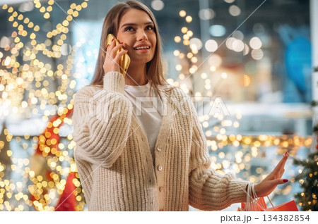 Magical decorations, talking by phone. New year shopping and presents. Woman is near the Christmas tree Magical decorations, talking by phone. New year shopping and presents. Woman is near the Christmas tree 134382854