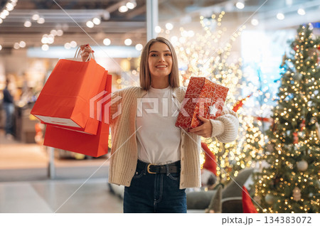 Cheerful facial expression, standing. New year shopping and presents. Woman is near the Christmas tree 134383072