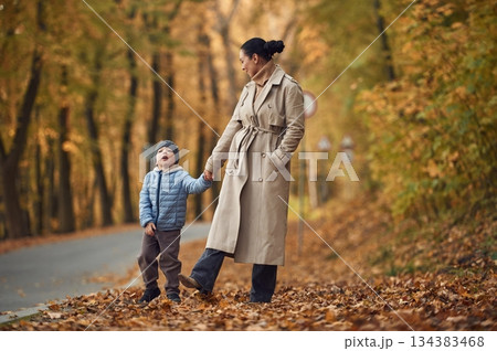 Mother with her son are having a walk in autumn forest near the road 134383468