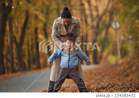 Fun times, behind the boy. Mother with her son are having a walk in autumn forest near the road 134383472