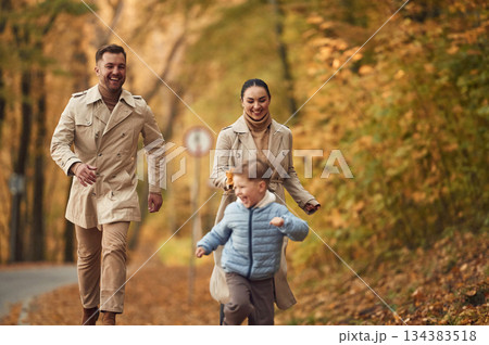 Boy is running forward. Happy family are together in the autumn forest near the road 134383518