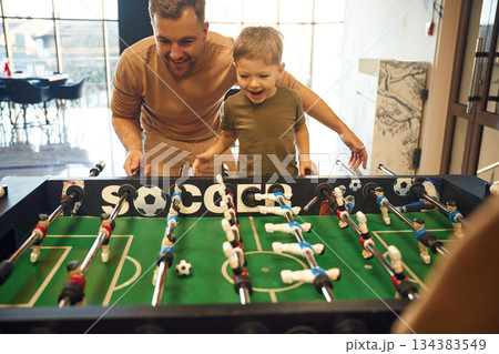 Conception of entertainment. Father and son are playing table football game indoors Conception of entertainment. Father and son are playing table football game indoors 134383549