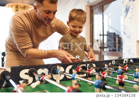 Teaching how to play. Father and son are playing table football game indoors 134384138