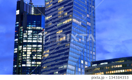 Office building in the evening with lightened workspaces. Modern, glazed skyscraper in financial district. Late hours in the office. Office building in the evening with lightened workspaces. Modern, glazed skyscraper in financial district. Late hours in the office. 134384353