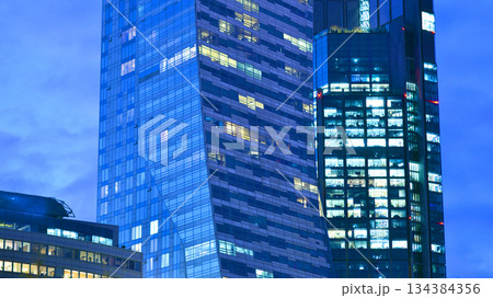 Office building in the evening with lightened workspaces. Modern, glazed skyscraper in financial district. Late hours in the office. Office building in the evening with lightened workspaces. Modern, glazed skyscraper in financial district. Late hours in the office. 134384356