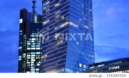 Office building in the evening with lightened workspaces. Modern, glazed skyscraper in financial district. Late hours in the office. 134384359