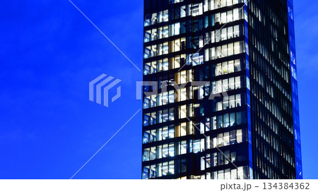 Office building in the evening with lightened workspaces. Modern, glazed skyscraper in financial district. Late hours in the office. Office building in the evening with lightened workspaces. Modern, glazed skyscraper in financial district. Late hours in the office. 134384362