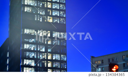 Office building in the evening with lightened workspaces. Modern, glazed skyscraper in financial district. Late hours in the office. 134384365