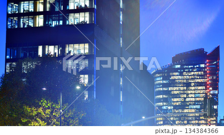 Office building in the evening with lightened workspaces. Modern, glazed skyscraper in financial district. Late hours in the office. 134384366
