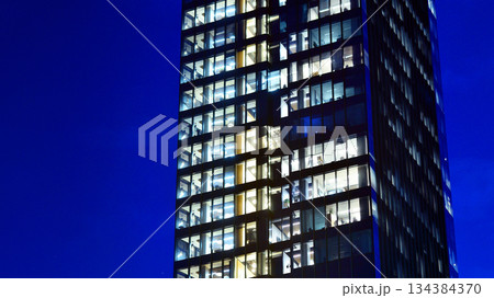 Office building in the evening with lightened workspaces. Modern, glazed skyscraper in financial district. Late hours in the office. 134384370