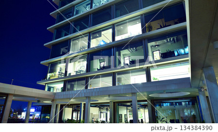 Office building in the evening with lightened workspaces. Modern, glazed skyscraper in financial district. Late hours in the office. Office building in the evening with lightened workspaces. Modern, glazed skyscraper in financial district. Late hours in the office. 134384390