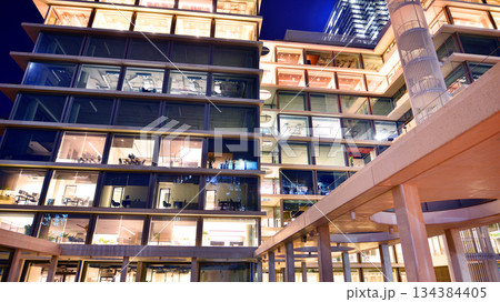 Office building in the evening with lightened workspaces. Modern, glazed skyscraper in financial district. Late hours in the office. Office building in the evening with lightened workspaces. Modern, glazed skyscraper in financial district. Late hours in the office. 134384405
